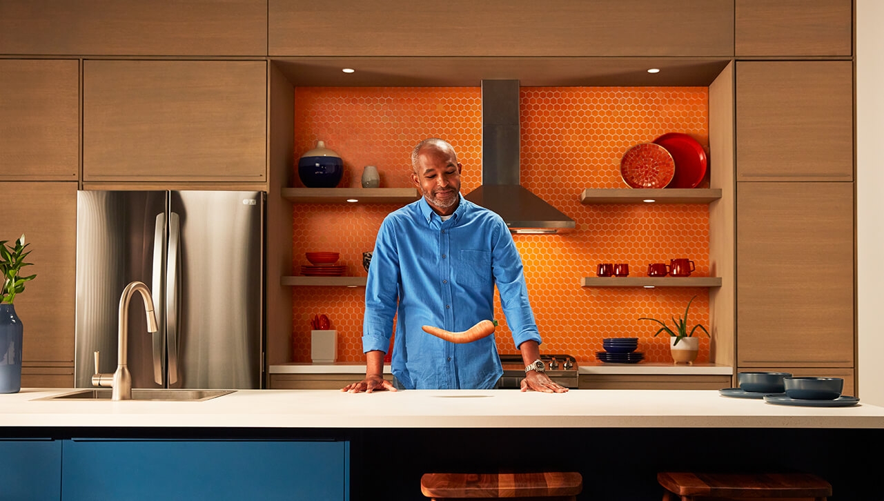 man standing in kitchen looking at a bent carrot